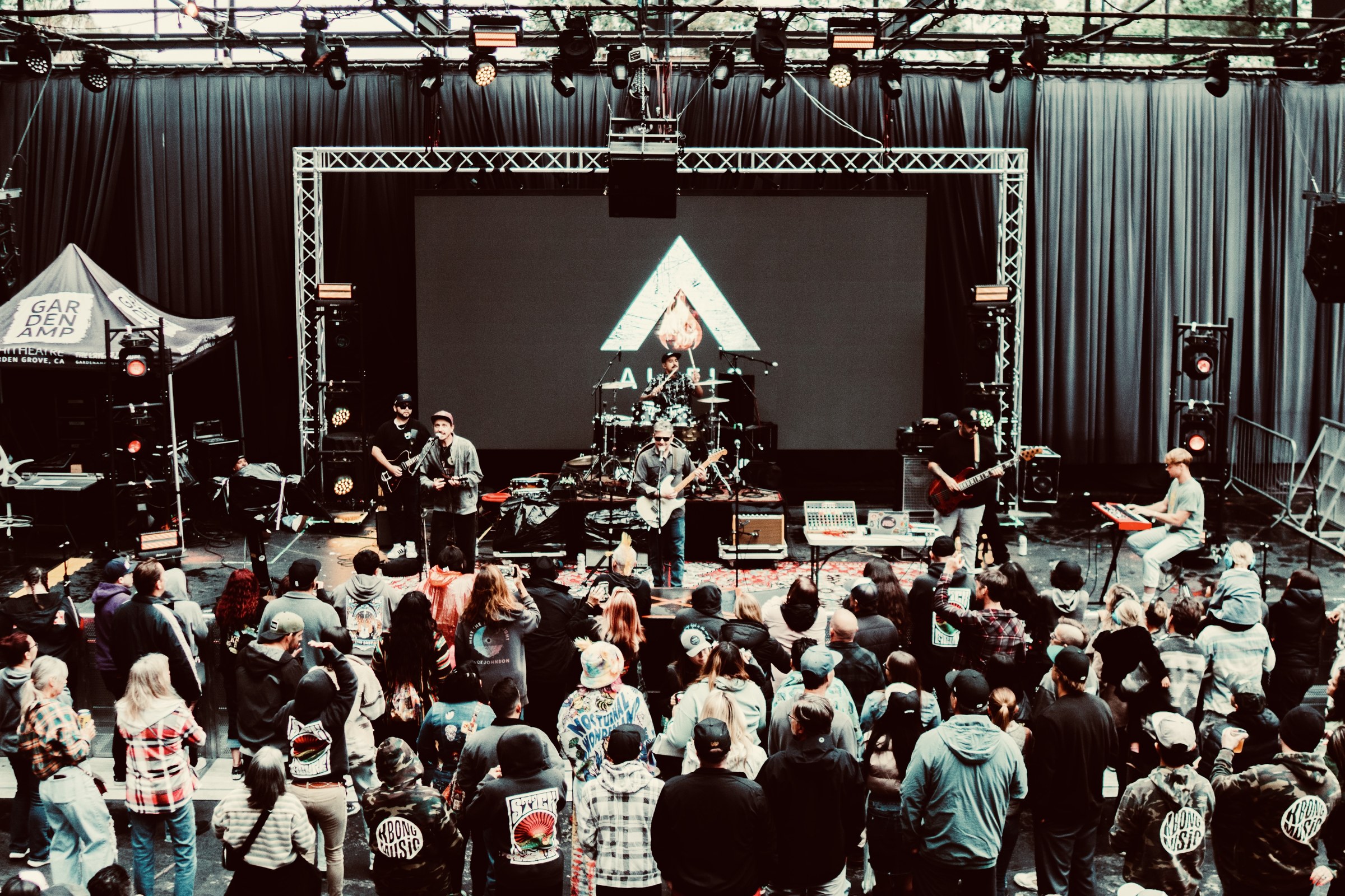 Alific and the full live band on stage at Garden Amp in warm evening light, with the audience gathered in front of the stage